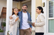 © fizkes - Positive couple of new homeowners and young Indian realtor woman standing outside of house, looking away, discussing apartment buying deal. Looking away, viewing backyard, neighborhood