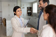 © fizkes - Cheerful young Indian real estate professional woman shaking hands with happy new homeowners, closing deal holding documents, smiling. Couple thanking realtor for successful apartment hunting