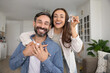 © fizkes - Excited young adult Hispanic couple of new happy homeowners posing for portrait in apartment, real estate property, showing key, looking at camera, laughing, hugging