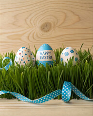 Poster - A vibrant Easter scene featuring three painted eggs nestled in lush green grass, each adorned with a 'Happy Easter' message. The eggs are complemented by a blue ribbon, adding a festive touch to the c