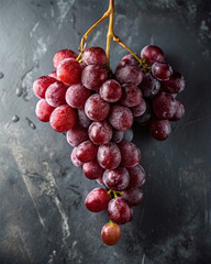 Poster - A close-up of a bunch of red grapes with water droplets on a dark, textured surface. The grapes are the main subject, with their vibrant red hue contrasting against the dark background. The texture of