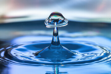 Poster - Captivating Water Droplet Creating a Colorful Splash in Serene Blue Surface