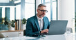 © peopleimages.com - Office, mature and businessman with laptop for email, financial report and auditing for corporate firm. Career, male person and accountant with tech for investment research, administration and smile