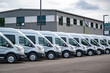 © vit - Compact gray cargo commercial mini vans standing in row on industrial warehouse parking lot waiting for the next local deliveries