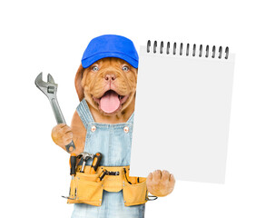 Poster - Funny Mastiff puppy wearing blue cap and denim overalls with tool belt shows empty list and wrench. Isolated on white background