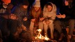 © kinomaster - Friends sitting around a campfire in the woods on a winter evening