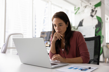thoughtful serious business project manager working at laptop in office, reading email letter, watch