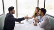 © fizkes - Multiethnic loving couple signing contract, shaking hands agent or sales manager, feel satisfied getting professional services, bank loan approval, buying new first property, making profitable deal