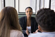© fizkes - Skilled African financial advisor provides information, consulting young married couple met in bank office. Female applicant passing job interview, answer questions seated in front of two HR managers