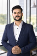 © fizkes - Serious young and ambitious Indian businessman, project leader dressed in formal jacket posing in modern workspace, exuding leadership, competence, experience, and professionalism. Corporate portrait