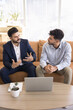© fizkes - Two millennial multiethnic businessmen seated on a sofa, engaged in serious business conversation, met in company office for negotiations or terms of deal, planning finances, budgeting or investment