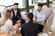 © fizkes - Overhead top view four young and ambitious professional team negotiate seated in modern office lobby, listening young European teammate presenting new project details, develop start up ideas. Teamwork