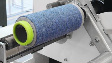 Poster - A blue and green yarn is being spun by a machine. The machine is made of metal and has a silver color