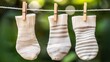 © Iurii - Hands carefully hanging striped socks on a clothesline in morning light with green leaves