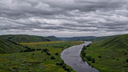 Wall Mural - Winding river through lush green hills under cloudy sky, panoramic landscape. Nature escape