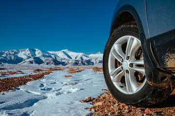 Fototapete - Car wheel on snowy mountains background, offroad travel
