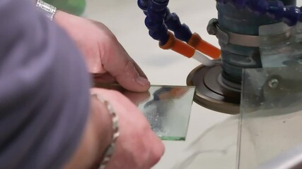 Poster - A craftsman processes the edges of glass pieces on a grinding machine at a glass manufacturing factory