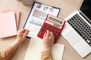 Fototapete - Female accountant with calculator, notebooks, laptop and financial graphics at table in office