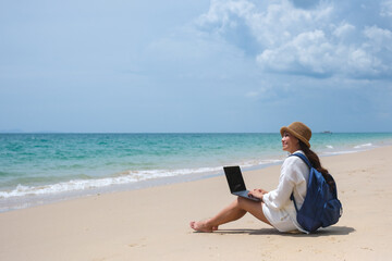 Wall Mural - a female traveler using and working on laptop computer while sitting on the beach