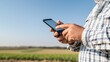 © Preecha - A rural farmer using a smartphone to access agricultural loans, with fields and a clear blue sky in the background, promoting financial inclusion, advertising style, copy space,