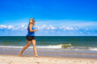 © Jacek Chabraszewski - Beautiful middle aged woman training running and listening to music in headphones on sandy beach in summertime. Side view
