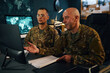 © DragonImages - Two military personnel in fatigues examining screen and documents in strategy room with maps on wall around. Engaged in detailed strategic planning without distractions