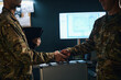 © DragonImages - Military personnel shaking hands in office with a computer screen and documents in background Highlighting cooperation and agreement between individuals in military environment