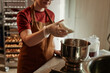 © Seventyfour - Cropped shot of female baker pouring coconut flakes from measuring cup into stainless steel bowl scaling ingredients for bread dough in bakehouse kitchen, focus on hands in vinyl gloves, copy space