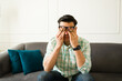 © AntonioDiaz - Exhausted latin male rubbing weary eyes, experiencing workplace stress while resting on living room sofa