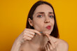 © New Africa - Beautiful woman plucking her facial hair with tweezers on orange background