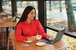 © New Africa - Woman with cup of coffee working on laptop at table in cafe