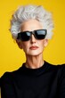 © Nataliya - Stylish elderly woman with gray hair wearing sunglasses against a yellow background