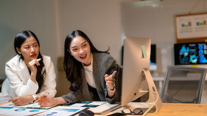 Poster - Two businesswomen pointing at desktop computer screen analyzing financial charts late at night in office