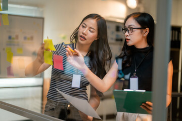 Poster - Businesswomen planning strategy using sticky notes on glass wall in office