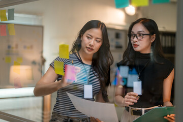 Poster - Businesswomen planning strategy using sticky notes on glass wall in office