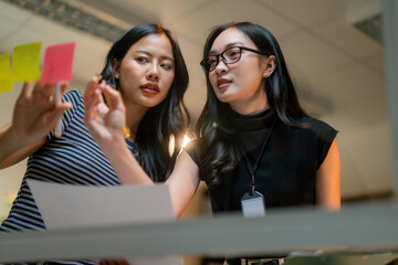 Poster - Businesswomen analyzing project planning using sticky notes on glass wall in the office
