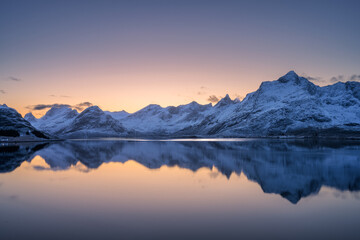 Wall Mural - calm water perfectly reflects snowy mountains during beautiful pink, orange sunset in lofoten island