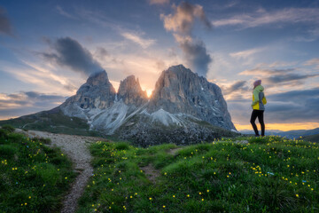 Wall Mural - girl on the hill with yellow flowers and green grass in beautiful alpine mountain valley at sunset i