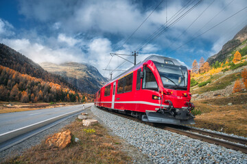 Wall Mural - red modern passenger train is moving on railway in swiss alps at sunset in autumn. landscape with tr