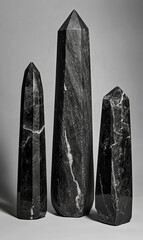 Fototapete - Black marble obelisks with geometric shapes and polished stone surfaces stand vertically in four varying sizes showcasing a minimalist monochrome design with sharp angles and smooth reflective