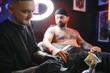 © Serhii - Professional tattoo artist makes a tattoo on a young man hand