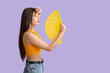 © Pixel-Shot - Young woman with hand fan suffering from heat on lilac background