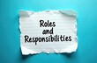 © Vadym - Roles, responsibilities written on torn paper piece over blue background. Conceptual symbol for team management, success strategy, corporate development. Pro duties, business tasks, personal growth.