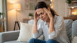 © Kunut - woman sitting on couch at home appears to be experiencing headache, showing signs of discomfort and stress