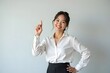Smiling asian business woman pointing up and looking at the camera over gray background.