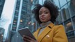 © liliyabatyrova - A stylish woman stands outdoors, confidently holding a tablet. Surrounded by towering skyscrapers, warm lighting reflects the urban landscape as twilight deepens