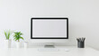 © Tatiana Nikulina - Minimalist workspace with a blank computer screen, plants, and stationery on a white desk, copy space