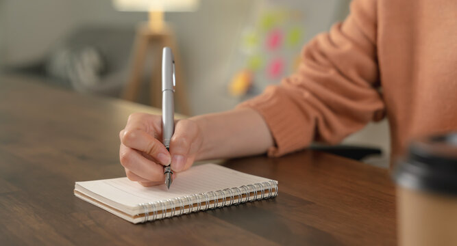 Woman hand writing on blank notebook on table in house.