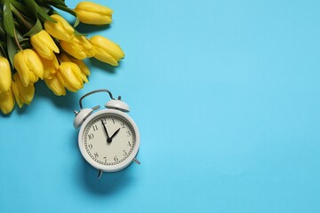 Poster - Spring time. Alarm clock and beautiful tulips on light blue background, flat lay. Space for text