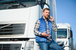 © Serhii - Professional driver using mobile phone while standing in front of his truck. Copy space